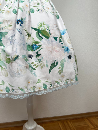 Detailansicht Rock, Bordüre mit großen cremefarbenen und hellblauen Blumen und grünen Blättern auf weißem Grund, hellblaue Spitze am Saum