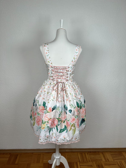 Rückansicht Kleid mit Trägern und gerüschtem Rock, weißer Stoff mit rosa Blumen, Bordüre mit großen Blumen in creme und rosa, rosa Schnürung am Rücken, rosa Spitze an Saum und Trägern