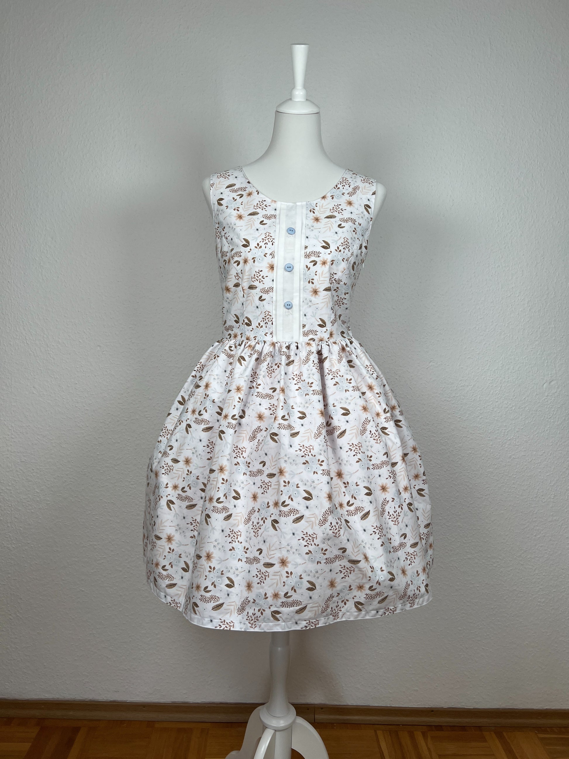 Trägerkleid, weißer Stoff mit Streublümchen in hellblau und Brauntönen, weiße dekorative Knopfleiste, hellblaue Knöpfe